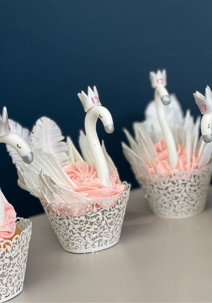 Three swan cupcakes with piped white wings against a navy background